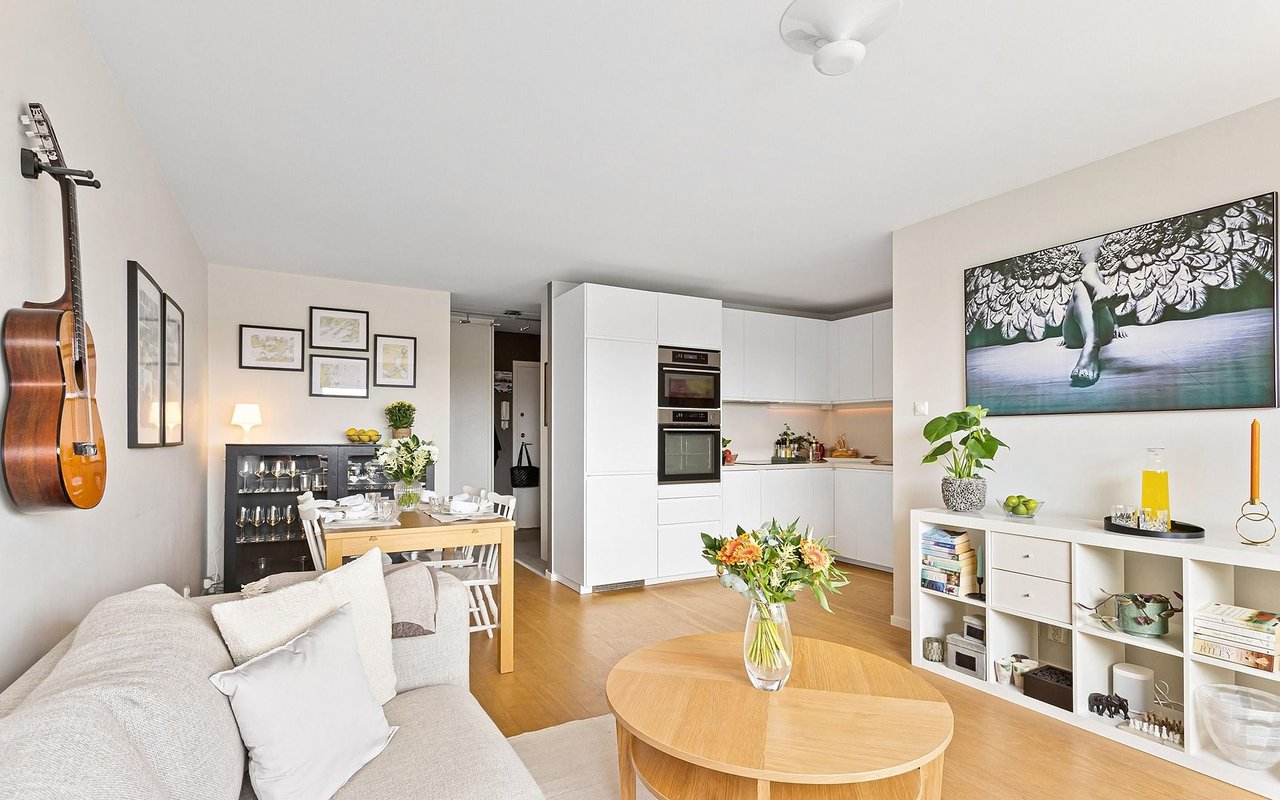 Open-plan living and dining area with white kitchen cabinetry and a wall-mounted guitar.