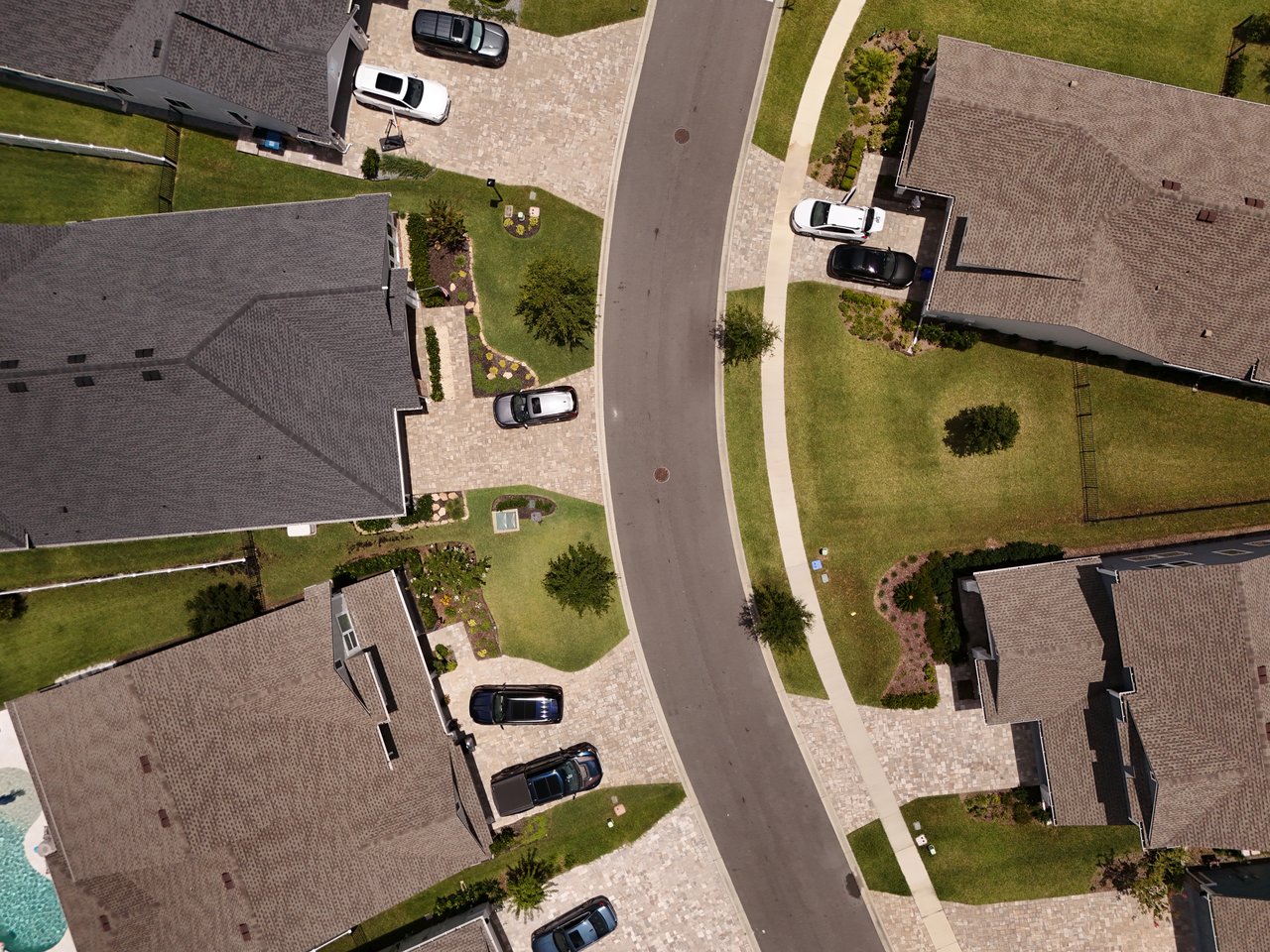 Aerial view of homes along a residential street with paved driveways and landscaped yards.