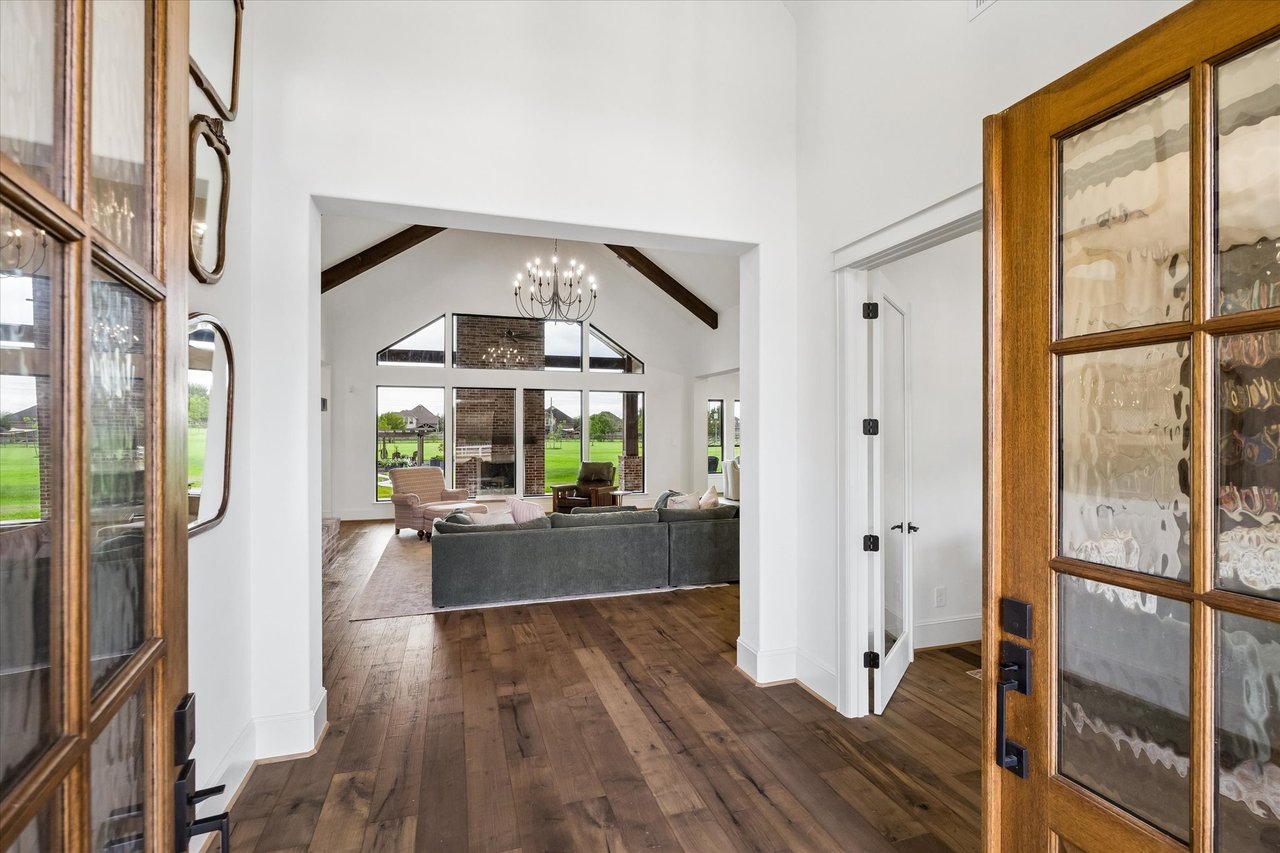 Living room with vaulted exposed-beam ceiling, wood floors, and large windows overlooking a green lawn.