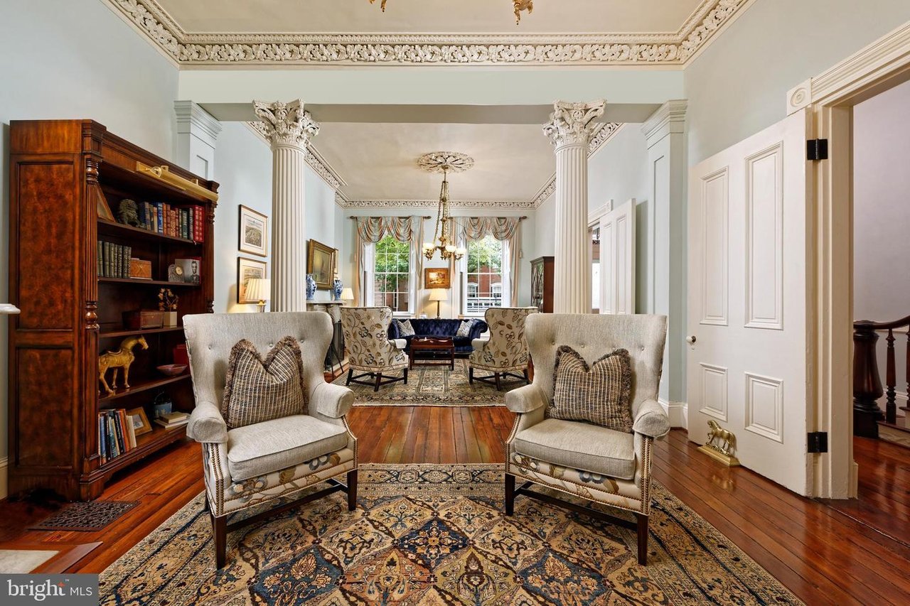 Formal living room with carved columns, ornate ceiling trim, patterned rugs, and upholstered chairs.