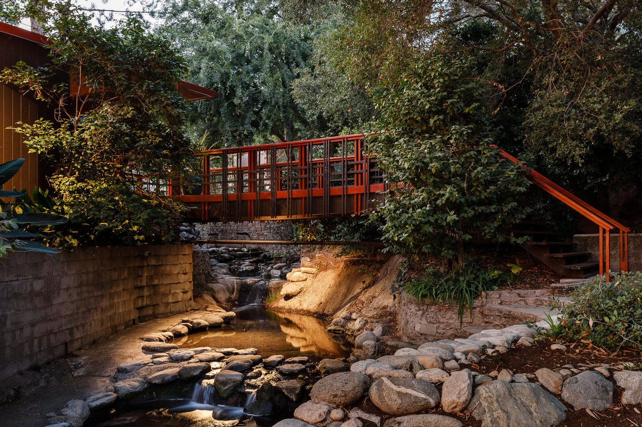 Wooden footbridge over a rocky creek in a wooded residential yard.
