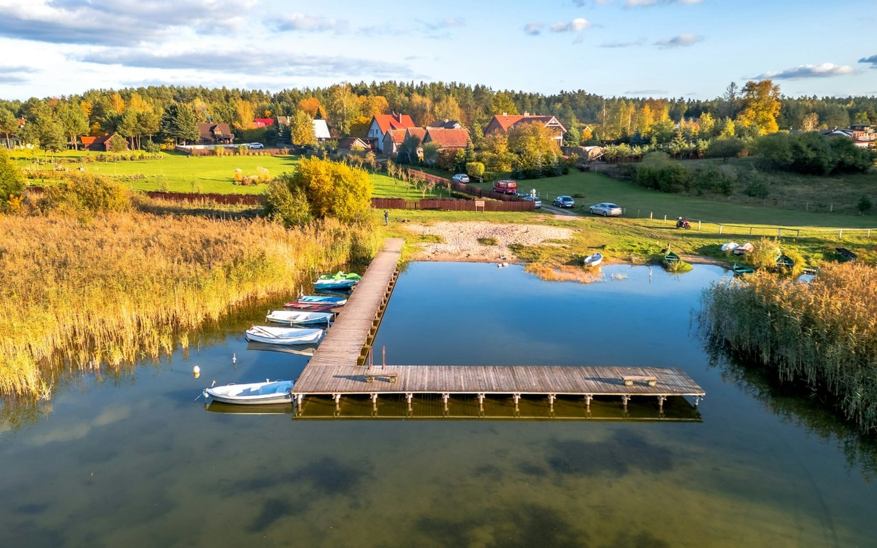 Waterfront neighborhood with a wooden dock and boats on a lake, backed by autumn-colored trees.