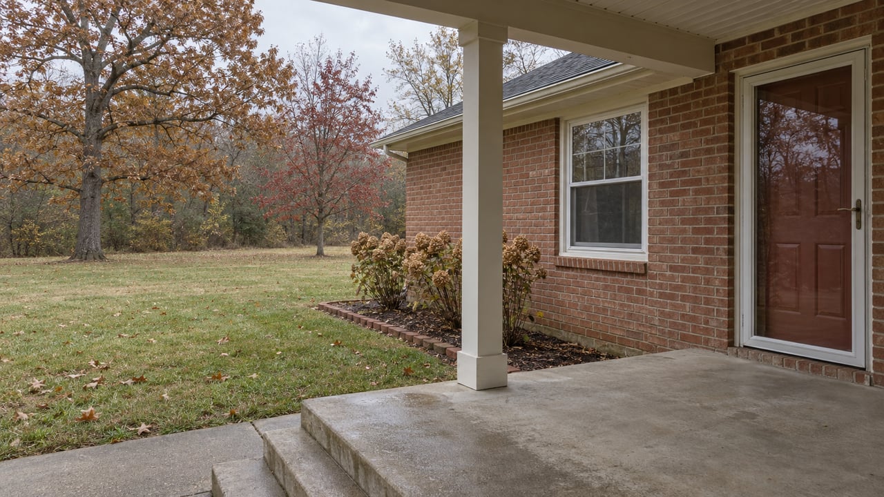 Weathered concrete porch and steps beside a red-brick ranch home, overlooking a deep autumn lawn with mature oak and maple trees.