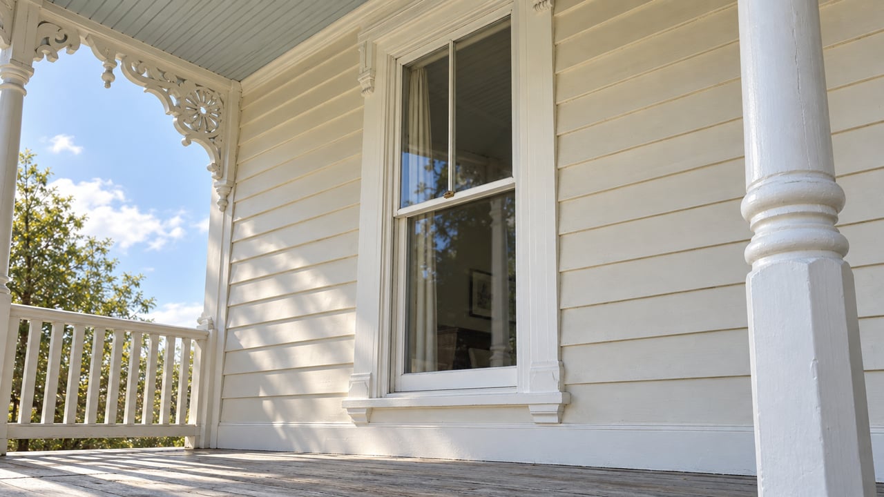 Cream clapboard porch corner with a narrow sash window, ornate bracket, and white turned post.