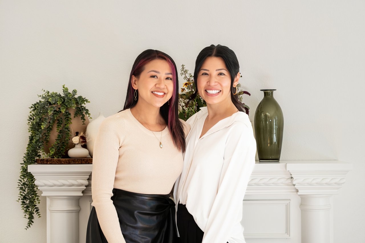 Kim Jade Tran and Michaela To standing together beside a fireplace.