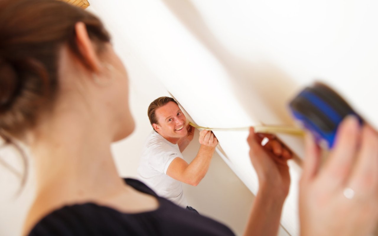 Two people measure a wall with a tape measure.