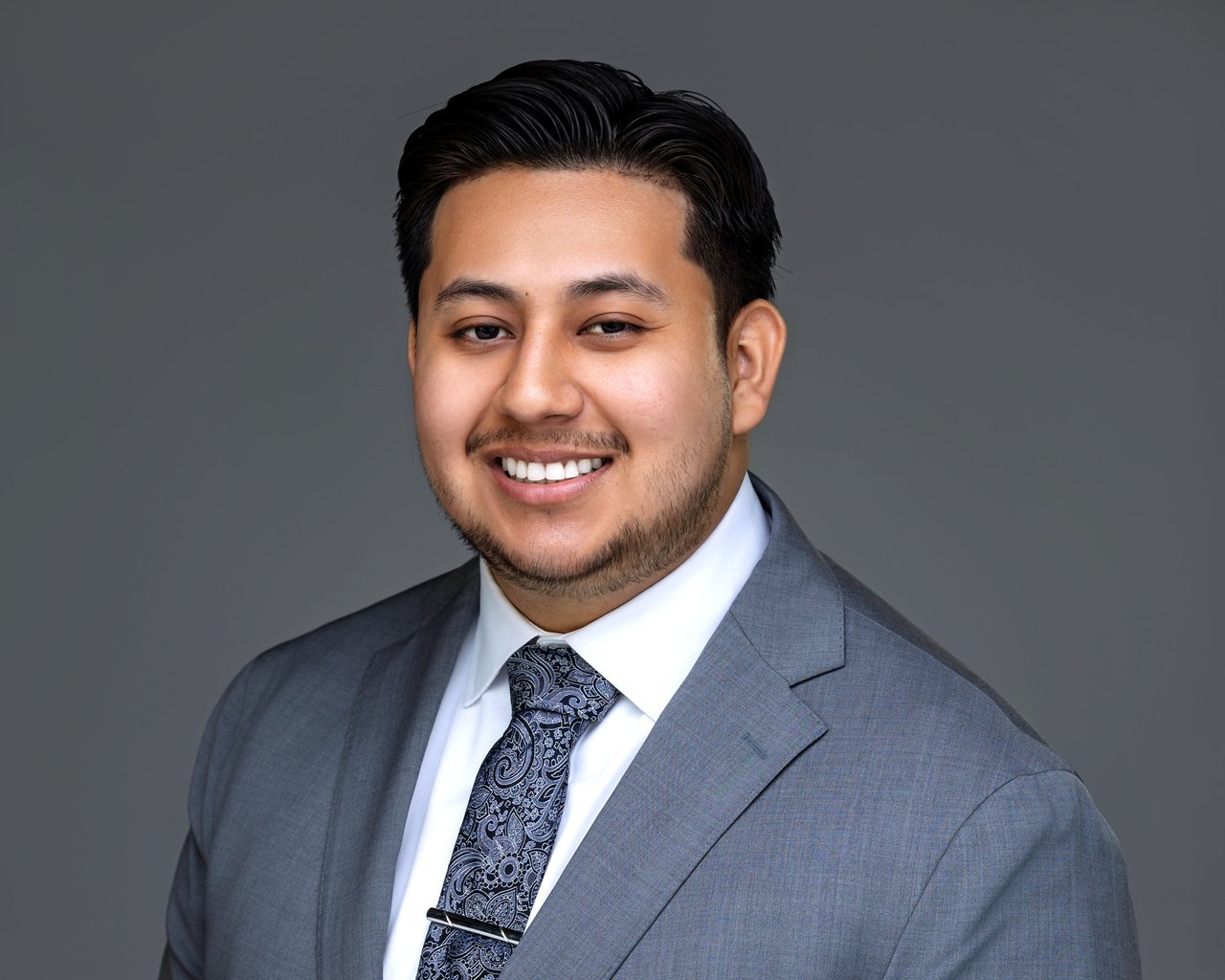 Eric Pacheco smiling in a gray suit and patterned tie.