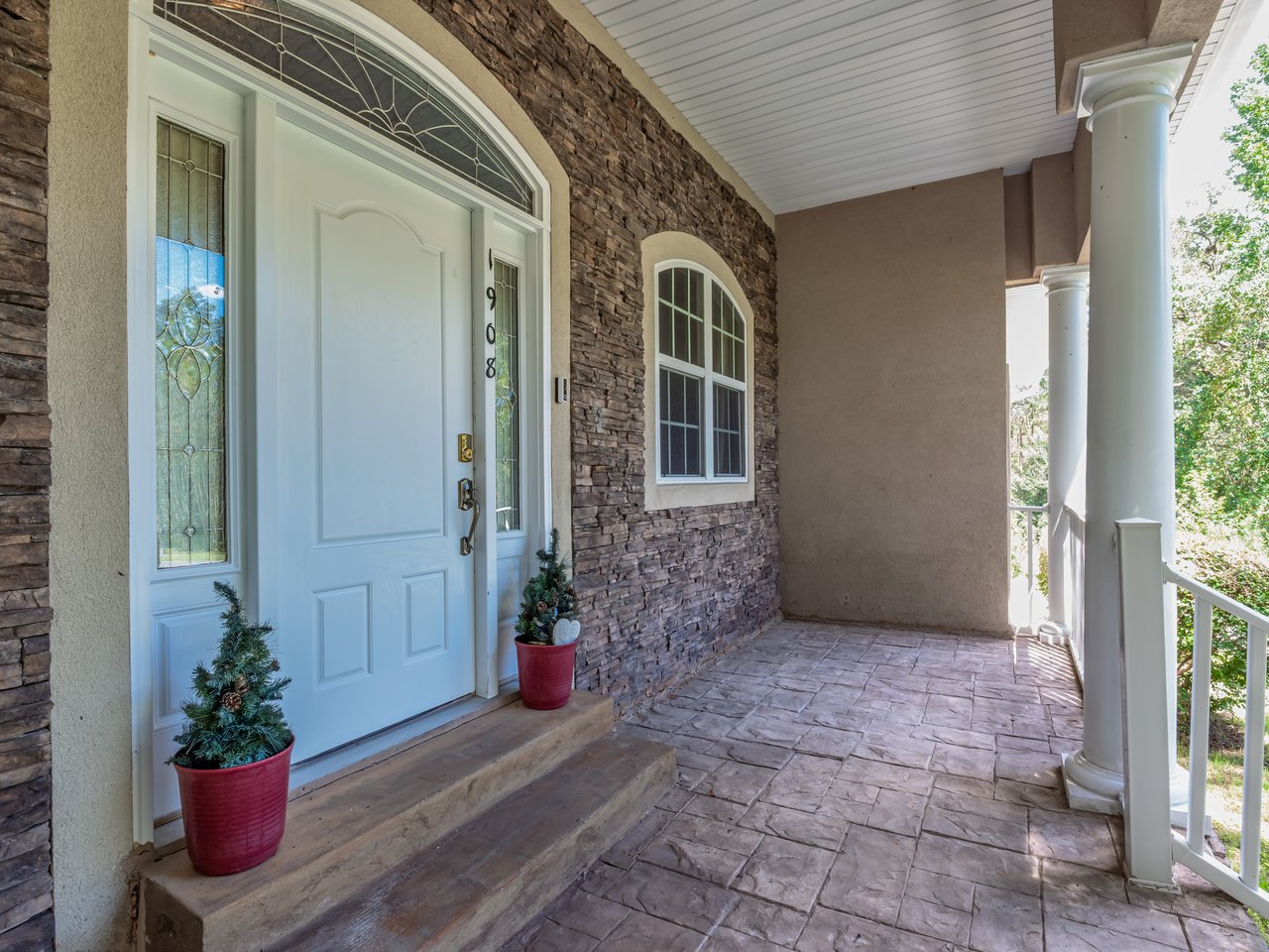 Stone-front home entrance with an arched glass door, tiled porch, and white columns.