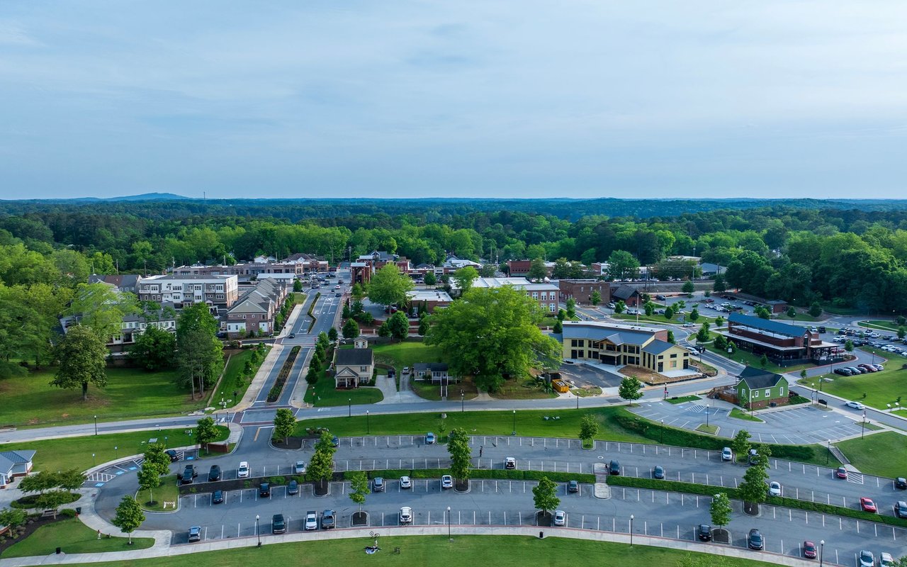 Aerial view of a town center with tree-lined streets and large parking lots.