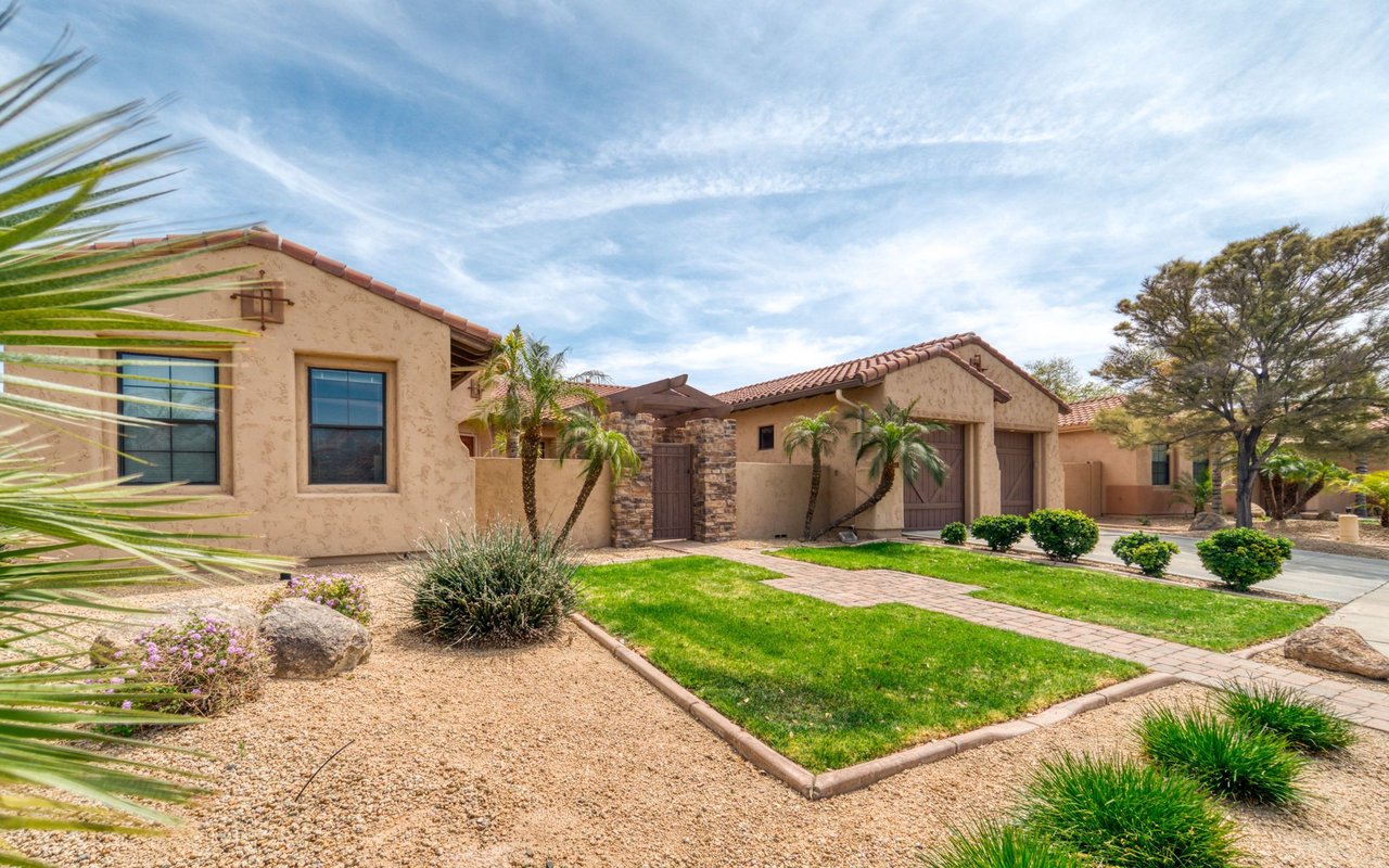 Tan stucco home with a red tile roof, stone entry, attached garage, and landscaped lawn.