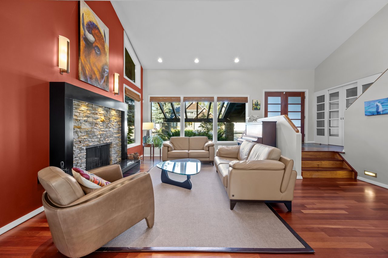 Living room with a stone fireplace, vaulted ceiling, leather seating, and large windows.
