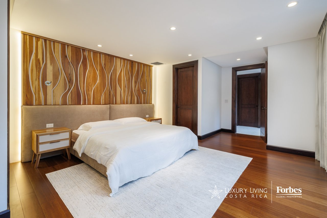 Penthouse bedroom with a white bed, sculpted wood feature wall, and dark wood flooring.