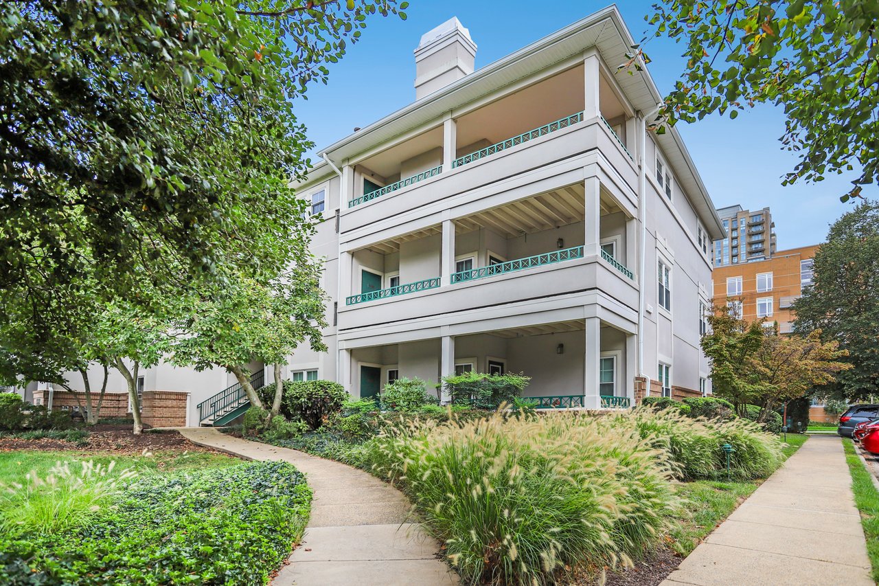 White multi-story residence with stacked balconies and teal railings, framed by trees and landscaped walkways.