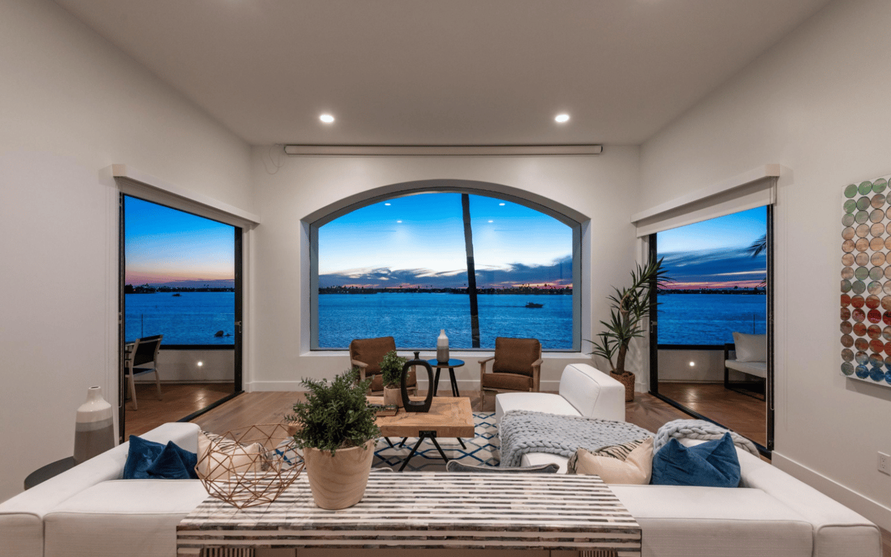  A modern living room with large windows that offer a panoramic view of a body of water at dusk. 