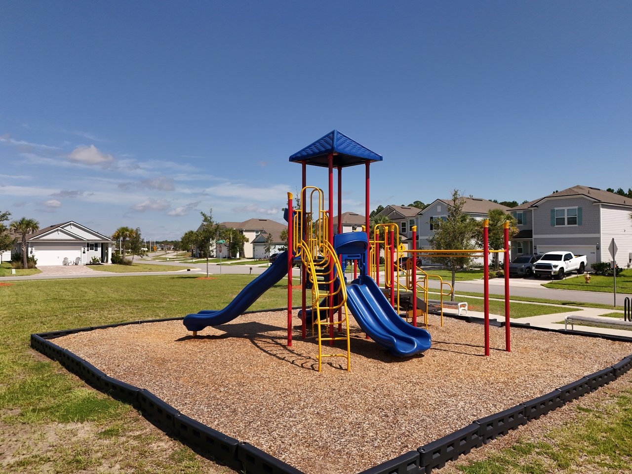 Neighborhood playground with blue slides and yellow climbing bars, with homes in the background.