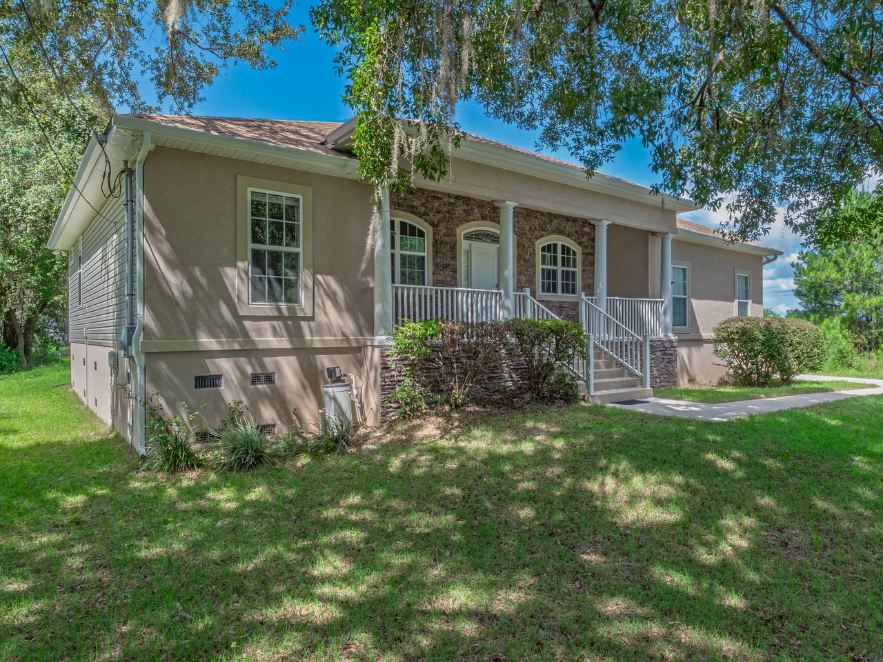Single-story home with a stone-accented entry and white-railed porch beneath mature trees.