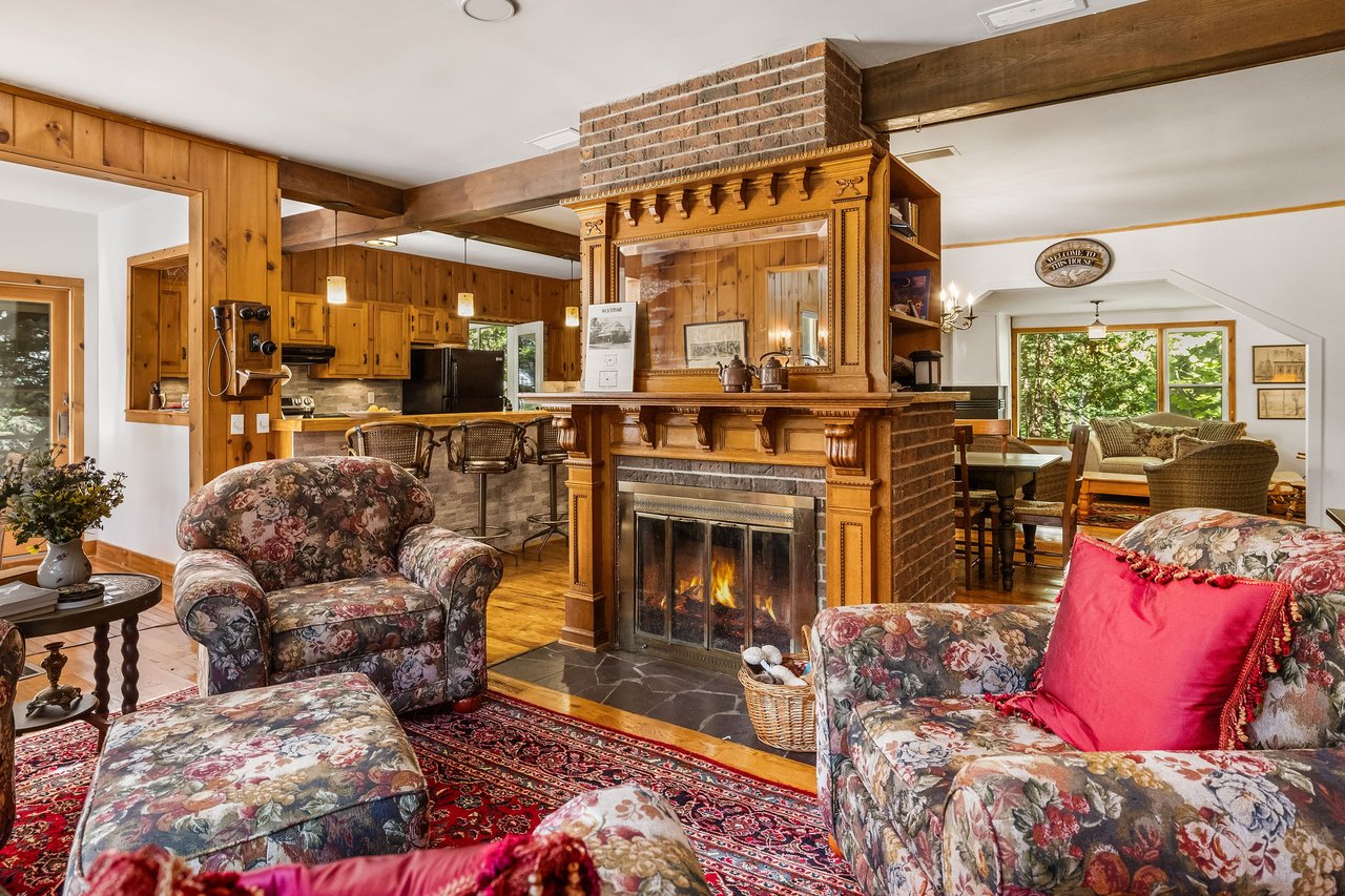Living room with an ornate wood-and-brick fireplace, exposed beams, and floral seating.