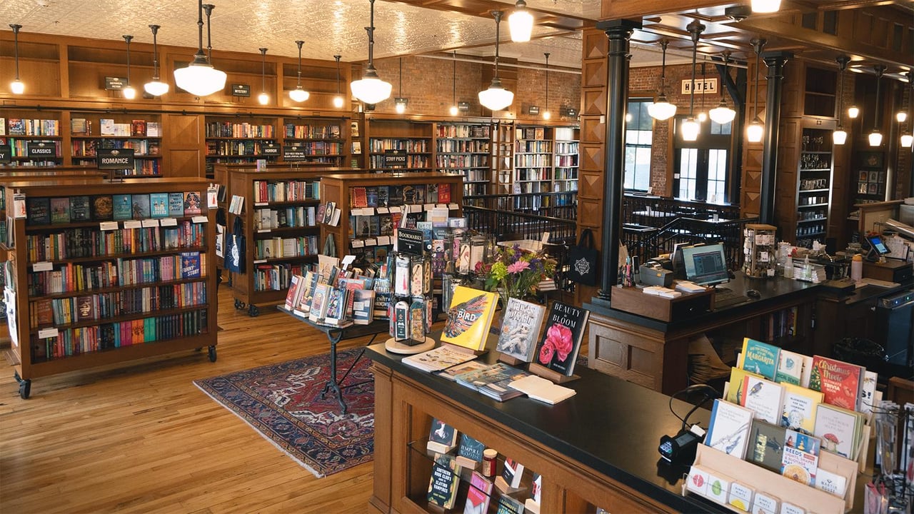 Bookstore interior with tall wooden shelves, a central book display, and a checkout counter.