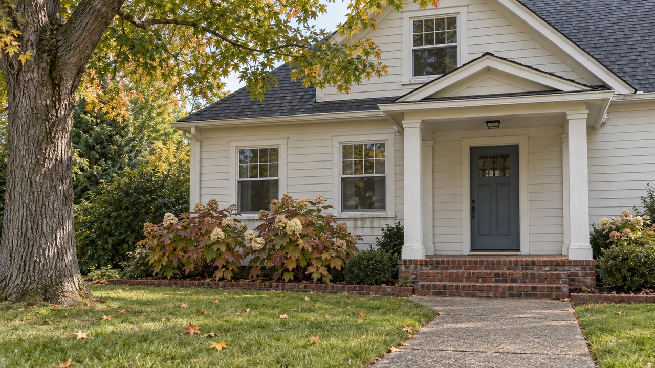 An established clapboard home with a brick porch, mature sugar maple and oakleaf hydrangeas in early autumn light.