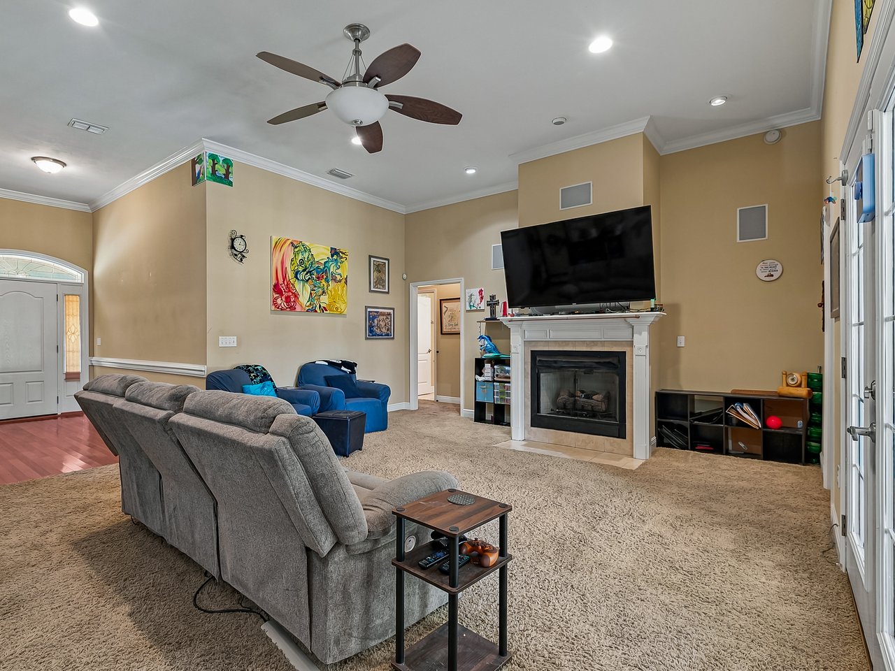 Living room with a gray sectional, blue armchairs, and a large television above the fireplace.