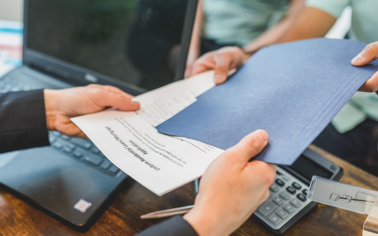 People exchange mortgage application paperwork over a laptop and calculator.