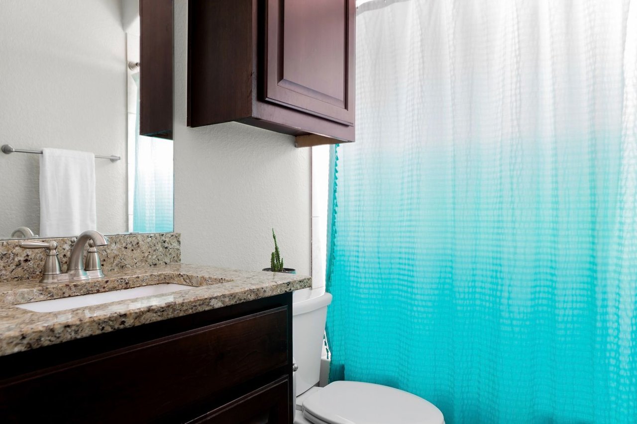 Bathroom with granite vanity, dark wood cabinets, and a turquoise shower curtain.