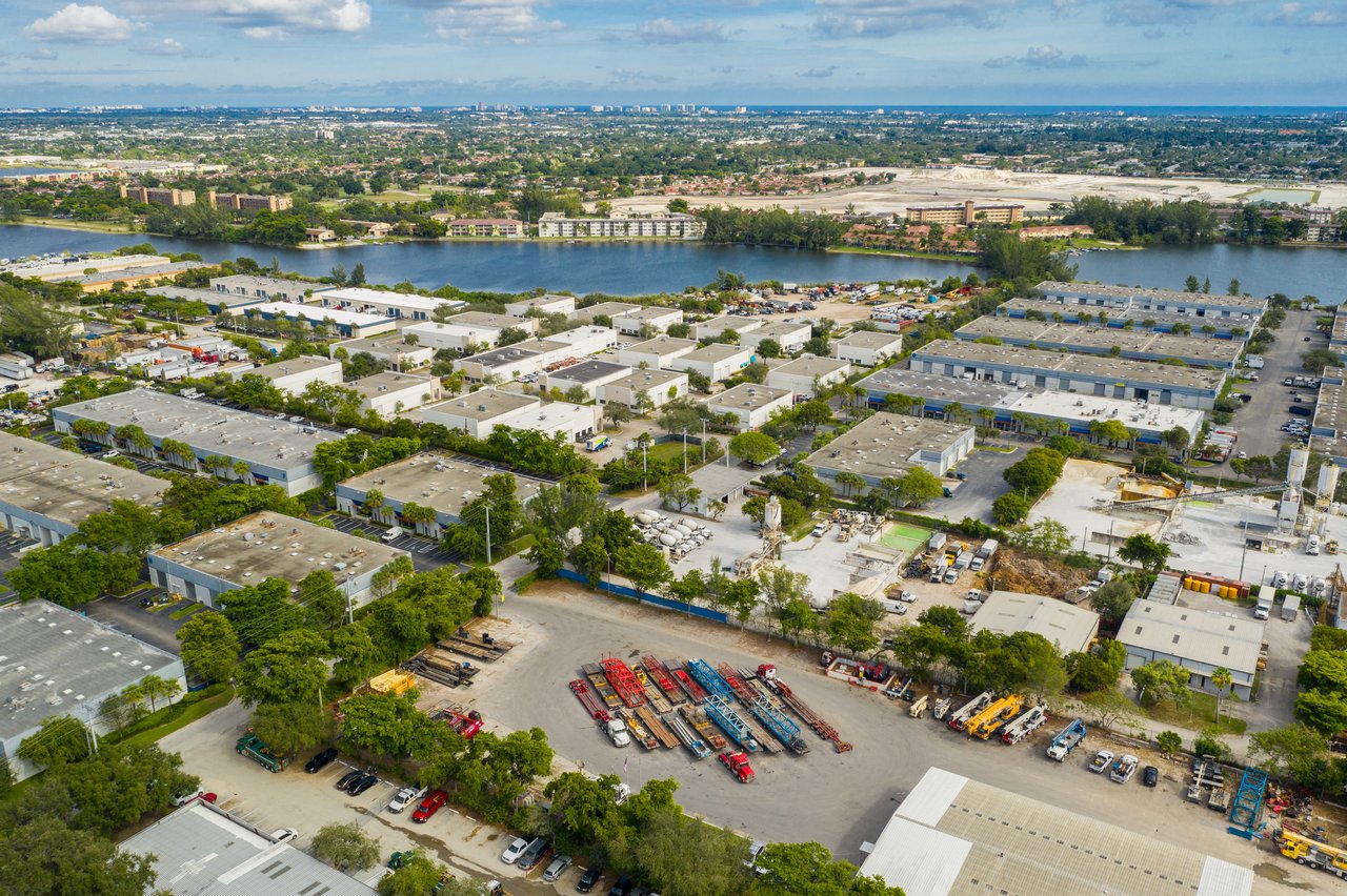 Aerial view of industrial waterfront buildings and equipment yards beside a broad waterway.