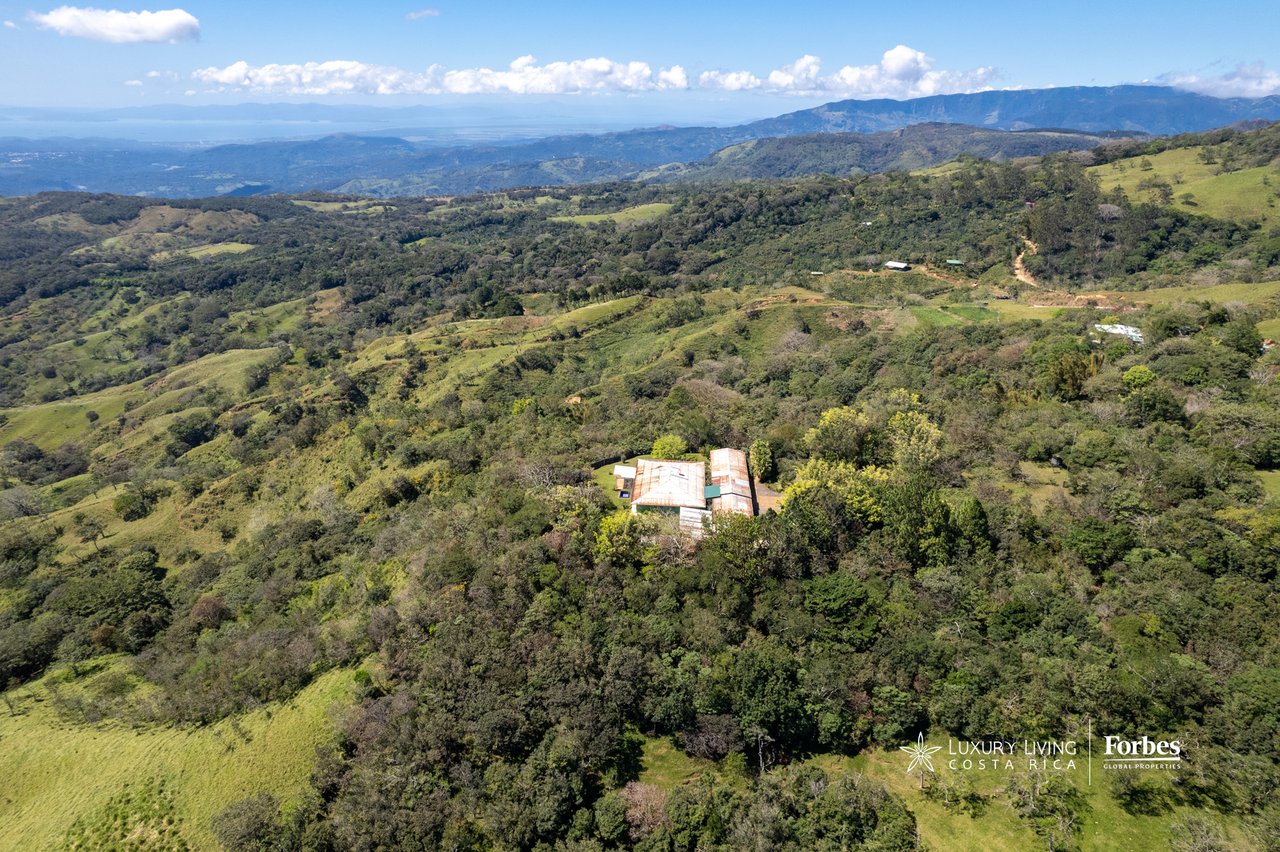 Aerial view of a mountain retreat amid wooded hills, with distant mountain ranges.