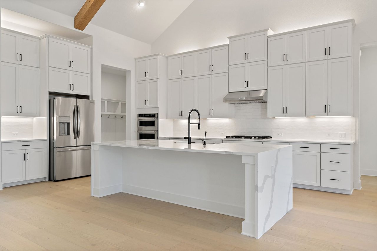 Kitchen view showing the quartz waterfall island, gas cooktop, and vent hood in the Cortaro home at 133 Mataro Cove, Dripping Springs, Texas.