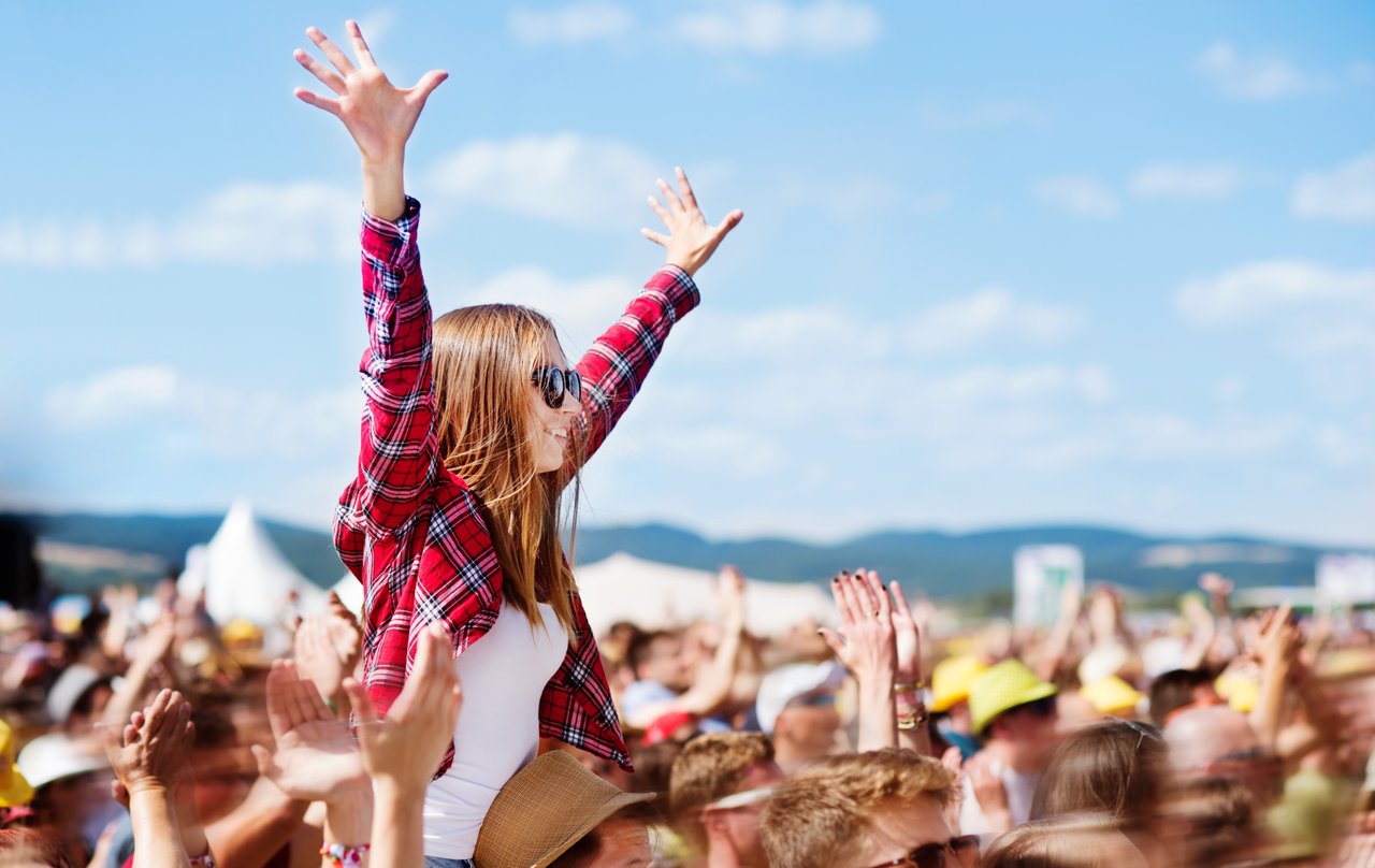 Smiling girl sitting on an adult’s shoulders in a crowded outdoor festival in Denver and attendees enjoying a summer celebration.
