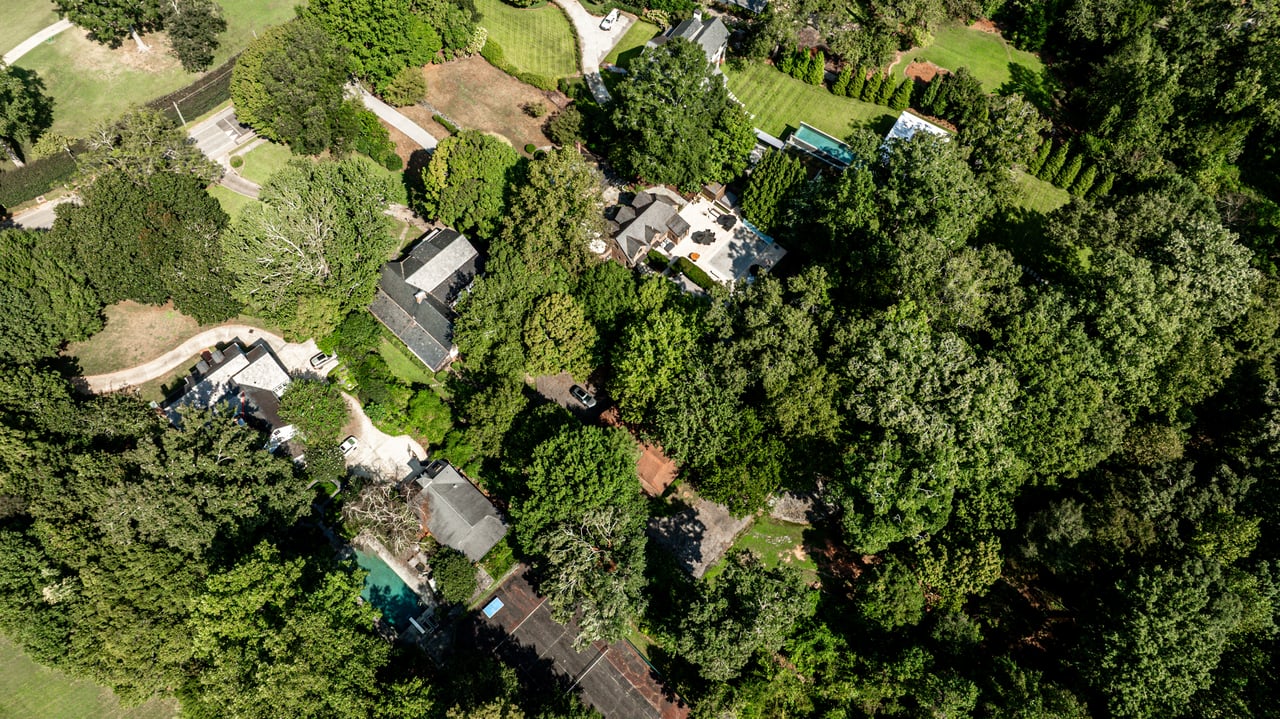 Aerial view of a wooded residential property with a swimming pool and surrounding homes.