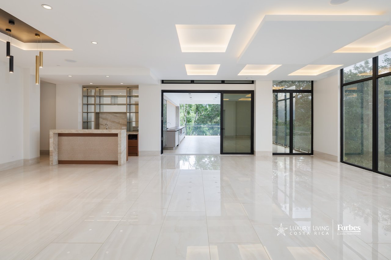 Open-plan apartment living area with a stone kitchen island and full-height glass doors overlooking trees.