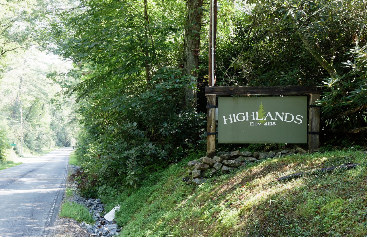 Highlands, North Carolina entrance sign surrounded by lush mountain forest along a scenic roadway, welcoming visitors to one of Western North Carolina's premier mountain communities.