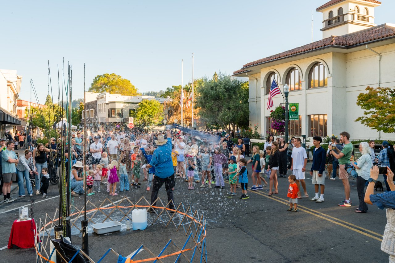 Crowds watch a water-spraying performer at a downtown San Anselmo street festival.