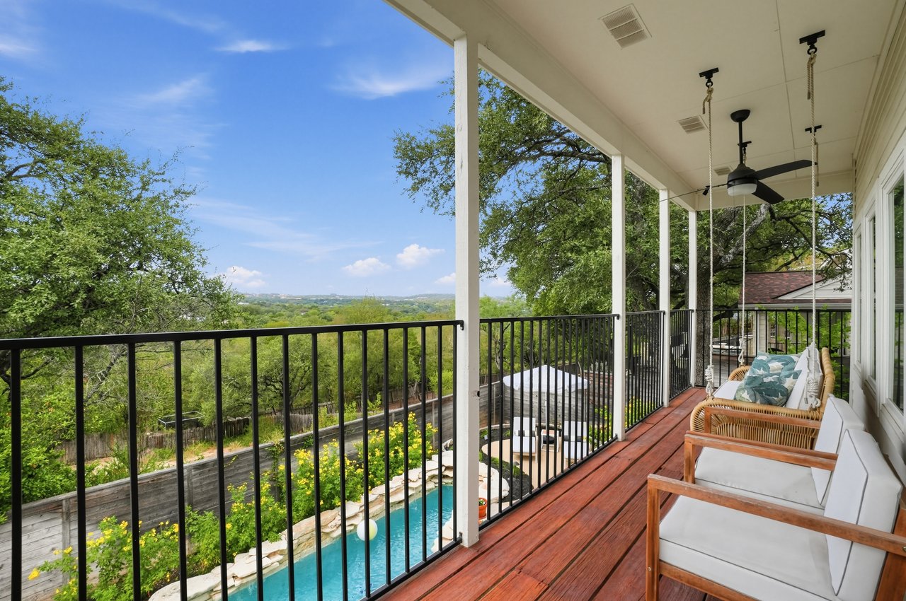 Covered wood deck with wicker seating and a ceiling fan overlooking a pool and wooded landscape.