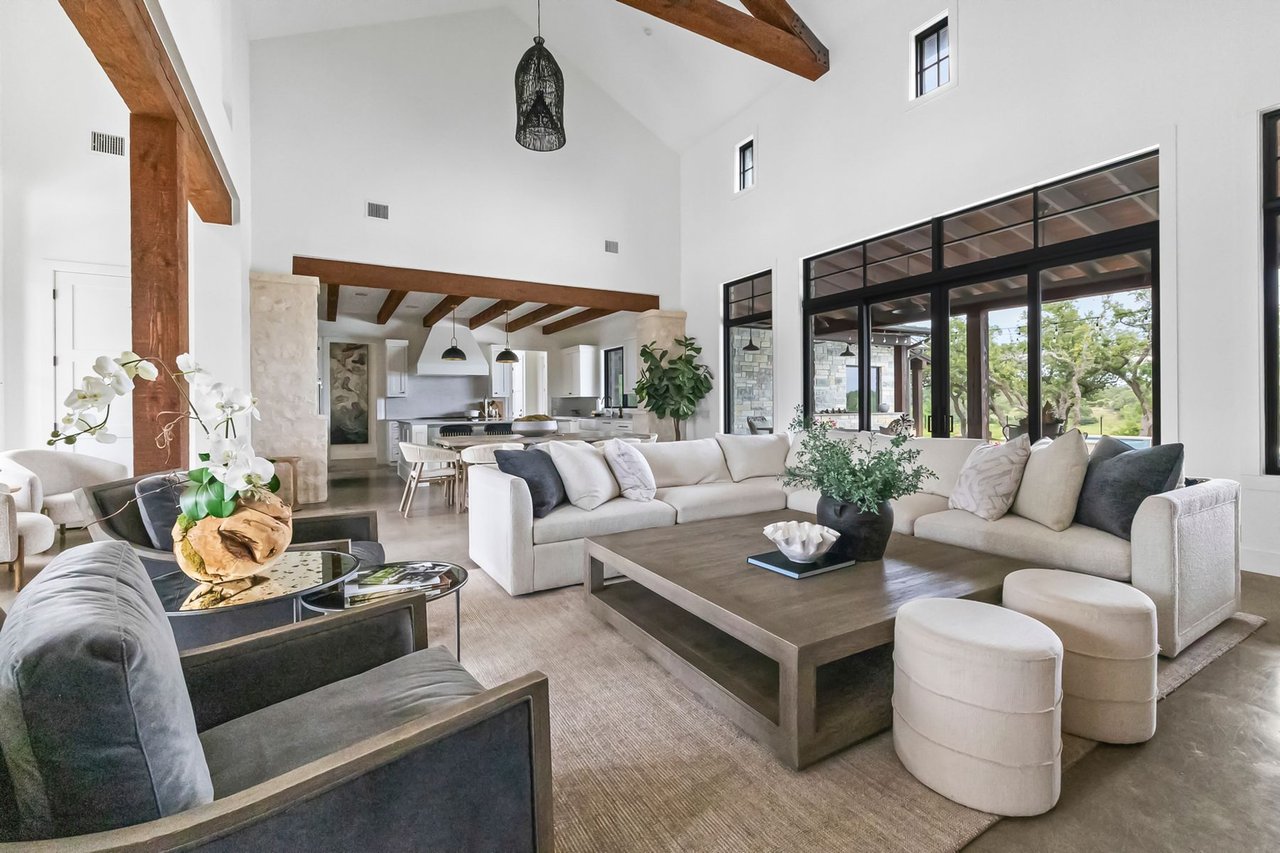 Great room with a vaulted, wood beamed ceiling and a wall of windows in this Creek Road Ranch home in Dripping Springs, Texas, designed by architect Kai Geschke.