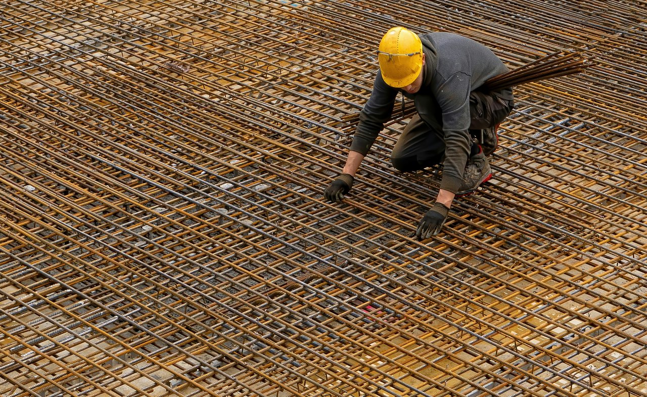 Construction worker in a yellow hard hat positions reinforcing bars across a foundation.