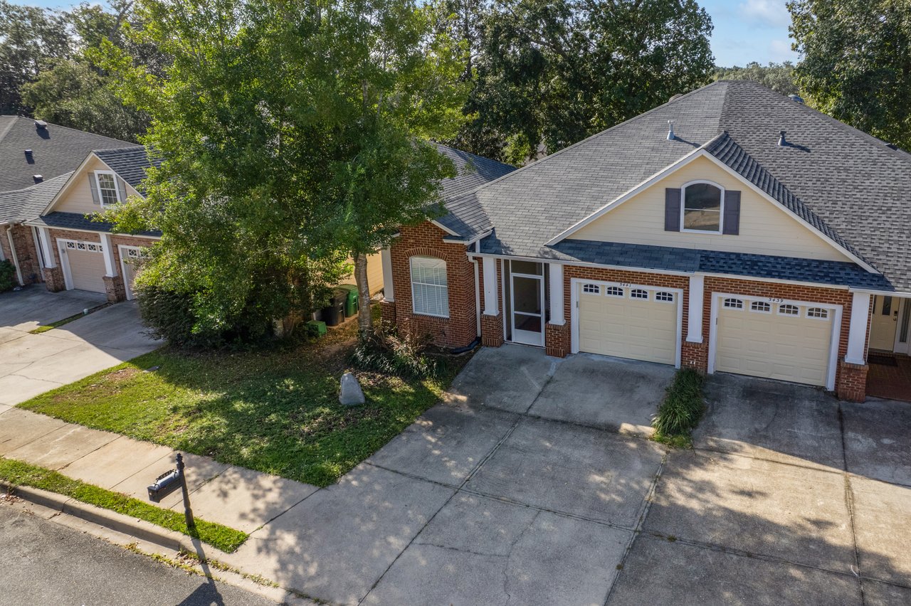 Front aerial view of 5441 Hampton Hill Circle, Tallahassee, Florida 32311 showing brick exterior, two-car garage, and shaded driveway.