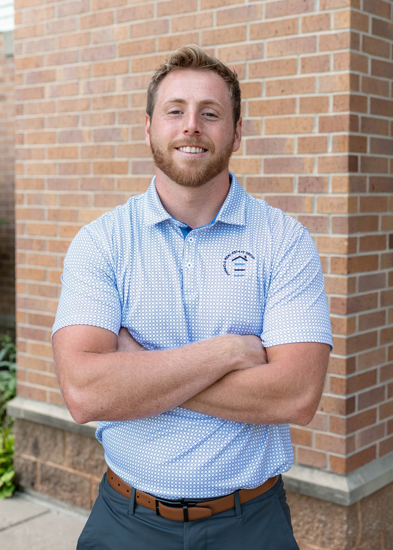 Jackson Chryst, smiling with arms crossed in front of a brick wall.