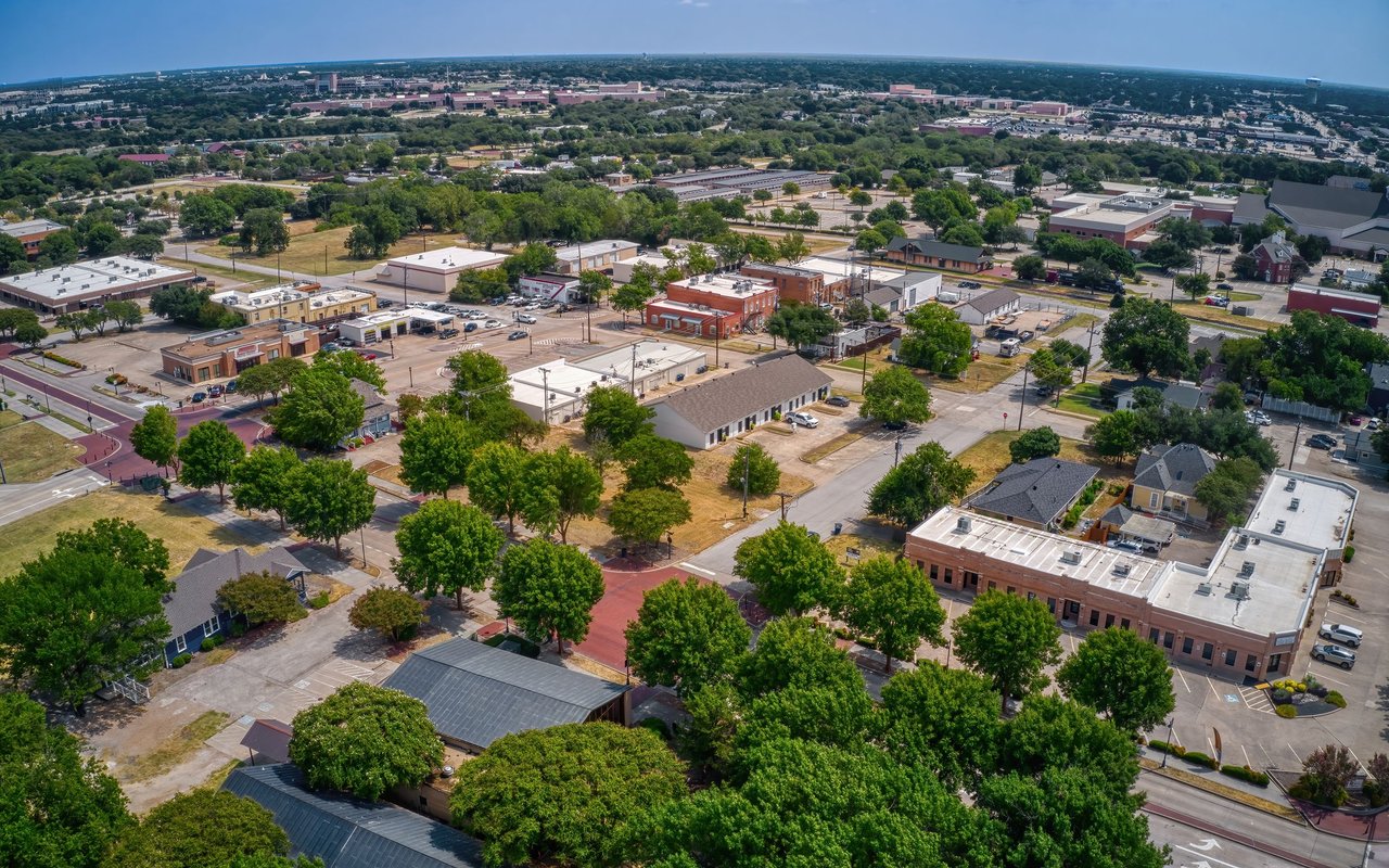 Aerial view of Montrose with tree-lined streets, homes, and low-rise commercial buildings.