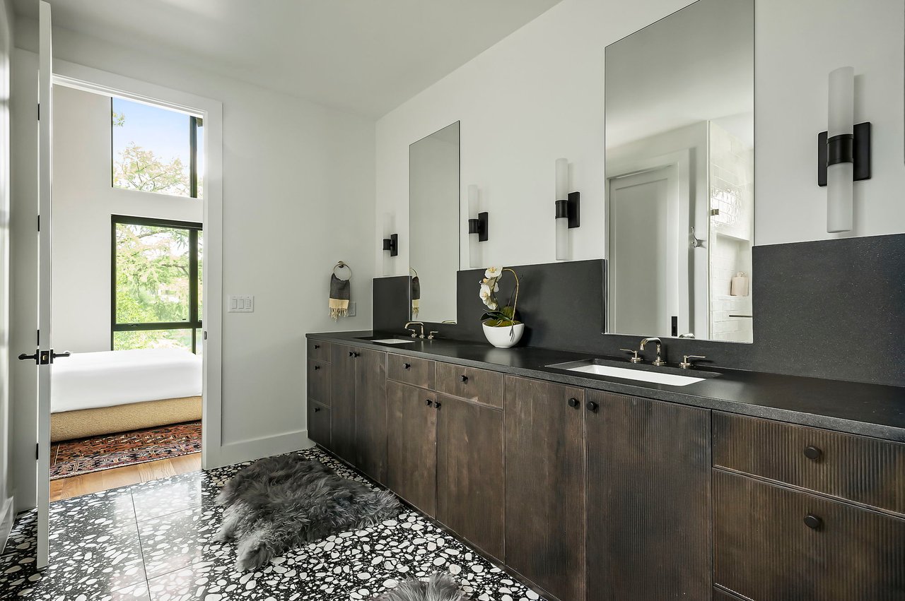 Primary bath with dual vanities, fluted floating cabinetry and black terrazzo flooring, designed by Kelley Design Group and built by Pecan Valley Custom Homes at 2403 Big Horn Drive, Austin.