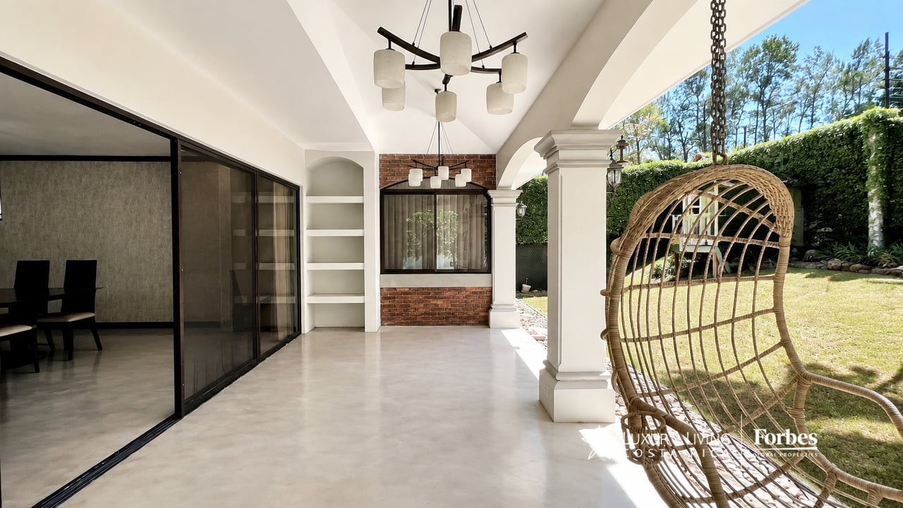 Covered terrace with white arches, a hanging wicker chair, and a garden lawn.