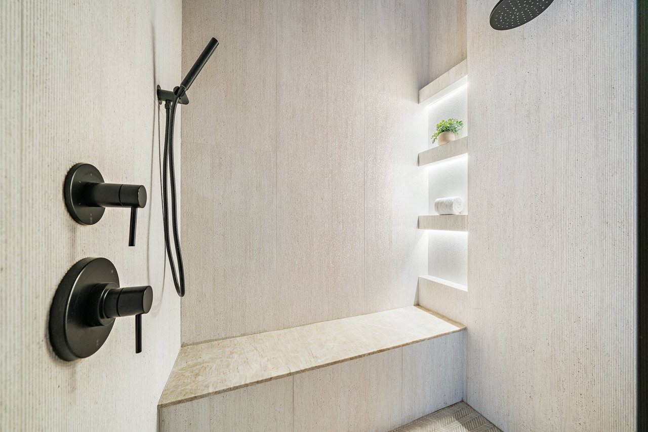 Walk-in shower with matte black fixtures, a stone bench, and illuminated display niches.