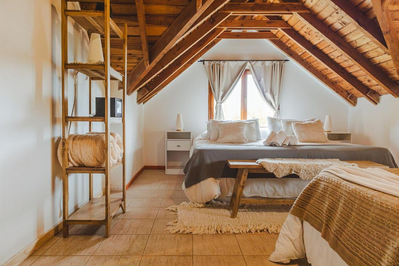 Attic bedroom with a large bed beneath exposed timber beams and open wooden shelving.