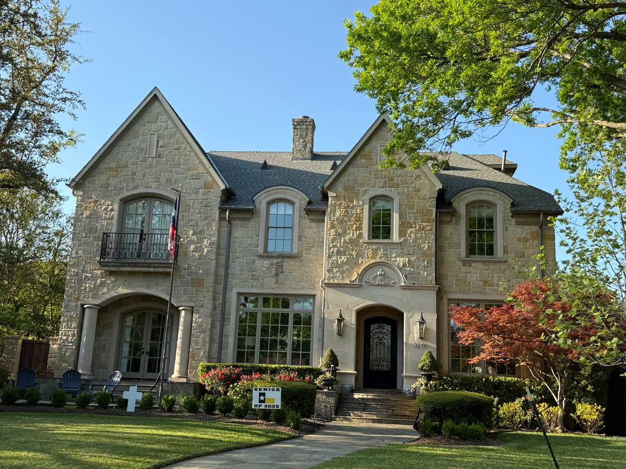 Two story luxury estate with twin gables with rough limestone walls with detailed landscaping including a red maple tree in the forefront.