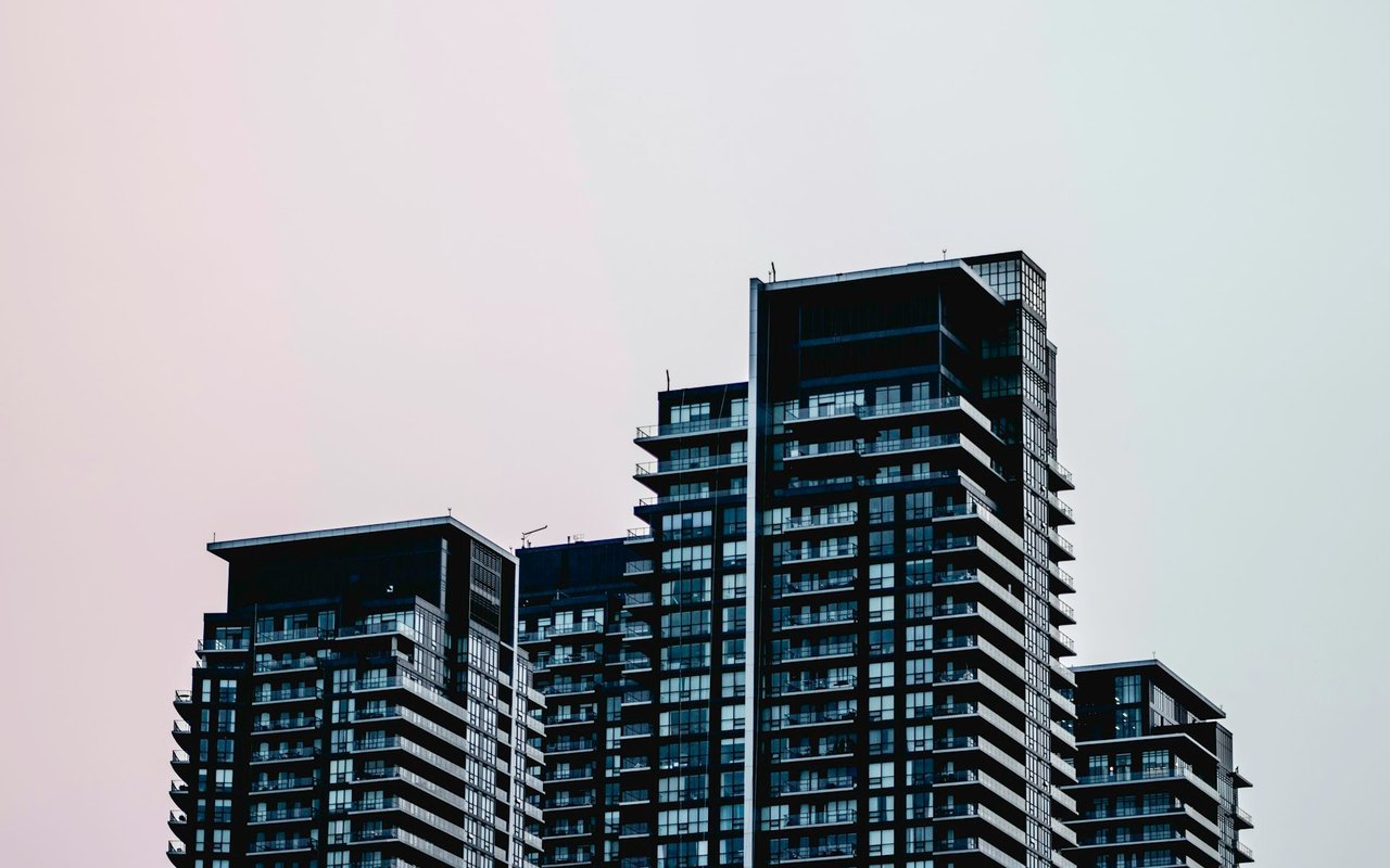Modern condominium towers with dark glass facades and balconies against a pale sky.