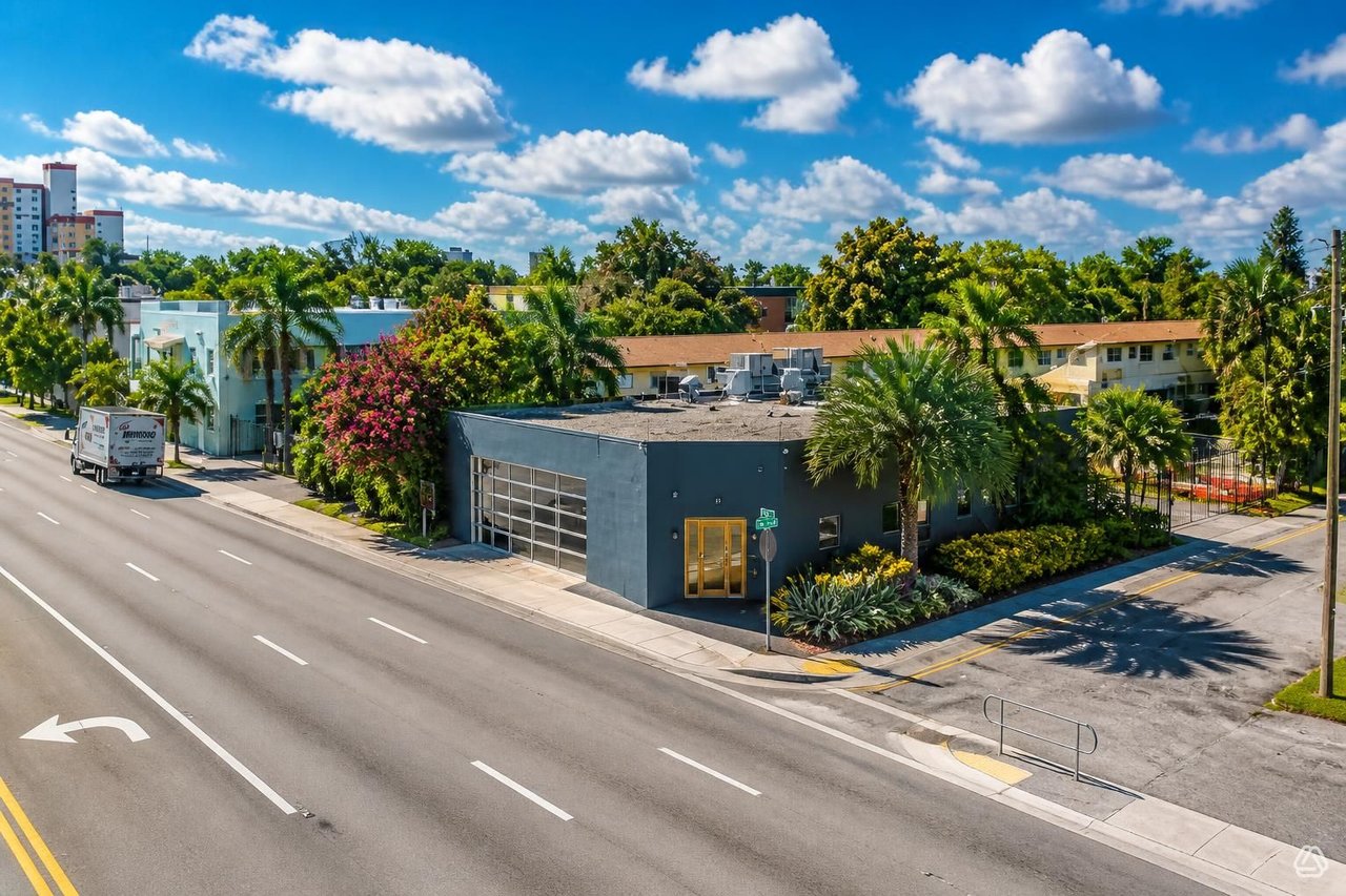 Modern dark-gray office building with yellow-framed entrance and palms, viewed from above a Florida street.