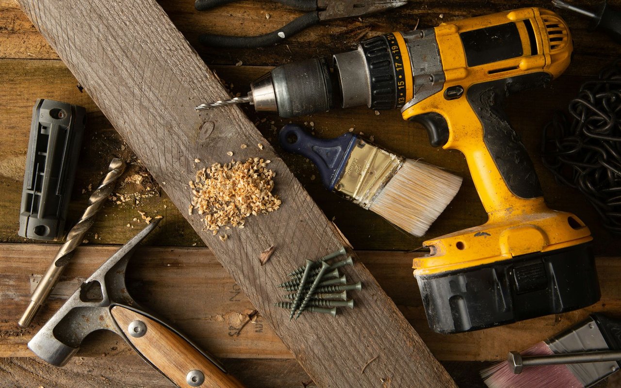 Cordless drill and assorted woodworking tools on a worn workbench.