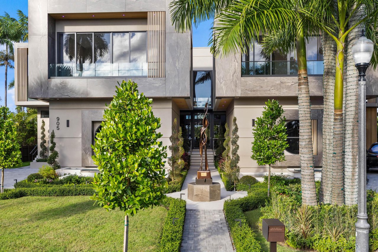 Modern two-story home with pale stone cladding, tropical palms, and a landscaped path to the entrance.