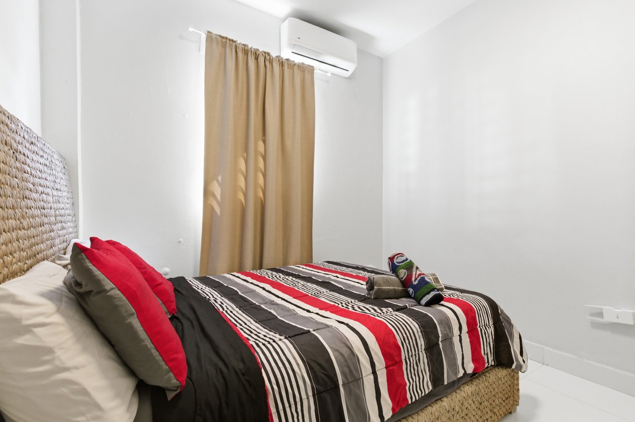 Bedroom with bold striped bedding, a woven headboard, and a wall-mounted air conditioner.